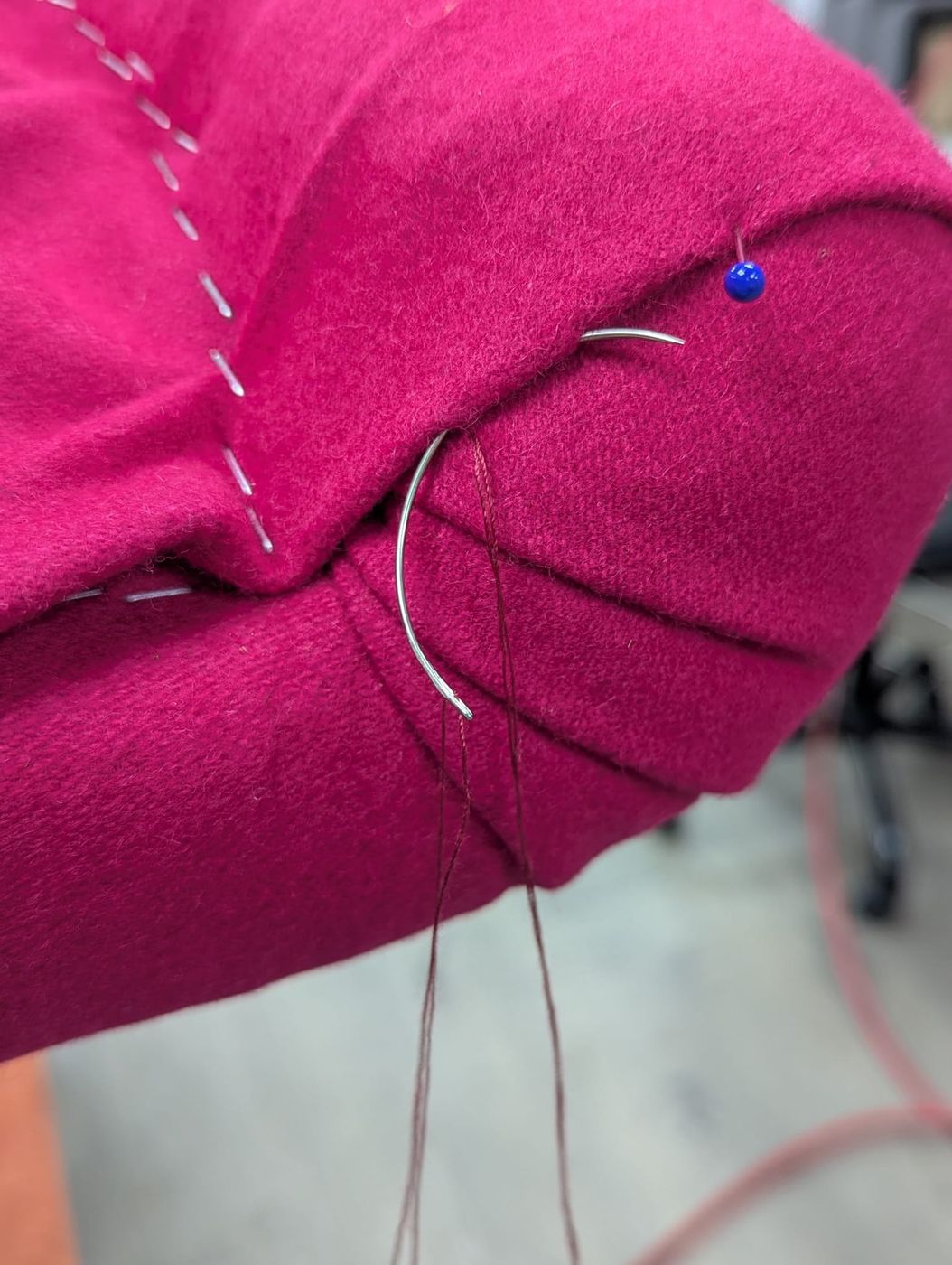 Hand-stitching the arm of a chair in fuchsia fabric